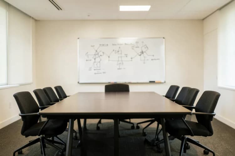 Sala de reunião com quadro branco e cadeiras, representando o ambiente de uma consultoria.