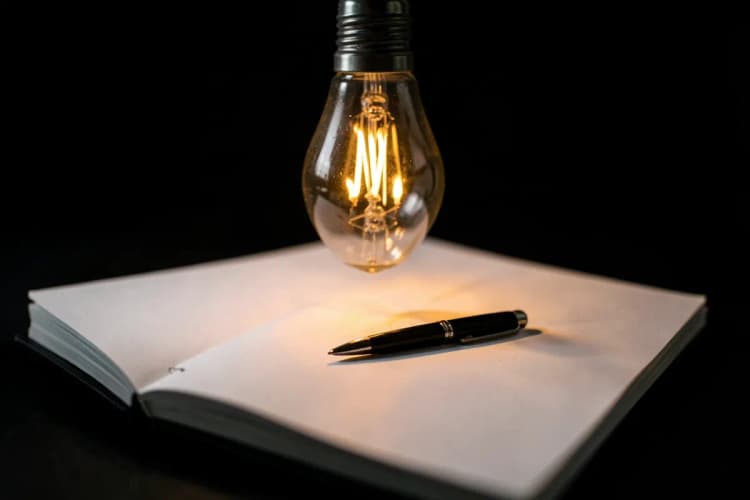 Lâmpada acesa sobre um bloco de notas com ideias escritas
