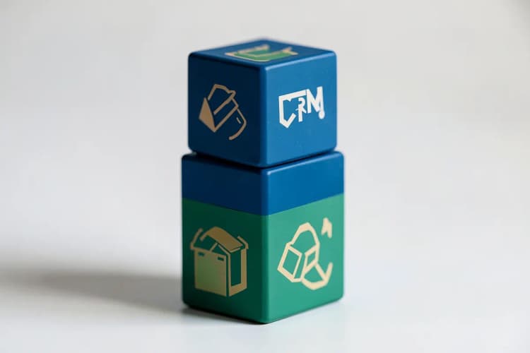 Uma ilustração de três cubos empilhados, cada um com um ícone diferente representando tipos de CRM (ex: operacional, analítico, colaborativo), em tons de azul e verde.