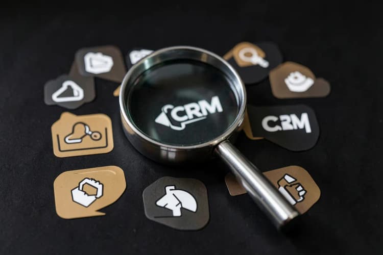 Uma lupa examinando diferentes ícones de software e ferramentas, representando a escolha de um CRM.
