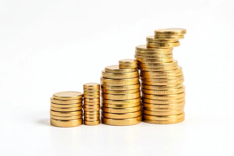 Gráfico de barras ascendente com moedas de ouro empilhadas em um fundo branco, representando crescimento financeiro.